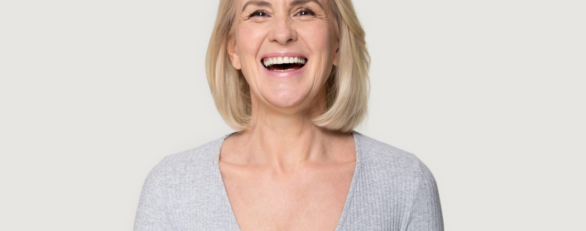 Head shot portrait overjoyed blond middle aged female smiling look at camera laughing feels happy pose isolated on grey studio background, advertise clinic procedure dental care prosthesis for seniors